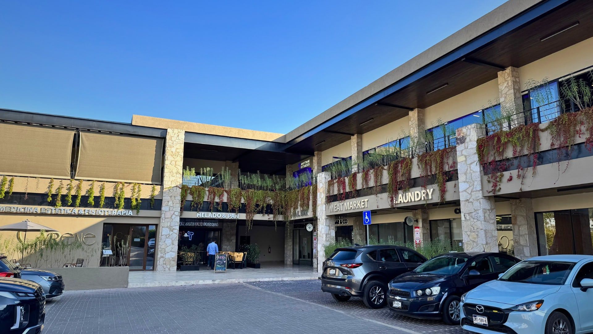 Fachada de Plaza Toscana con sus locales y estacionamiento a la luz de la tarde