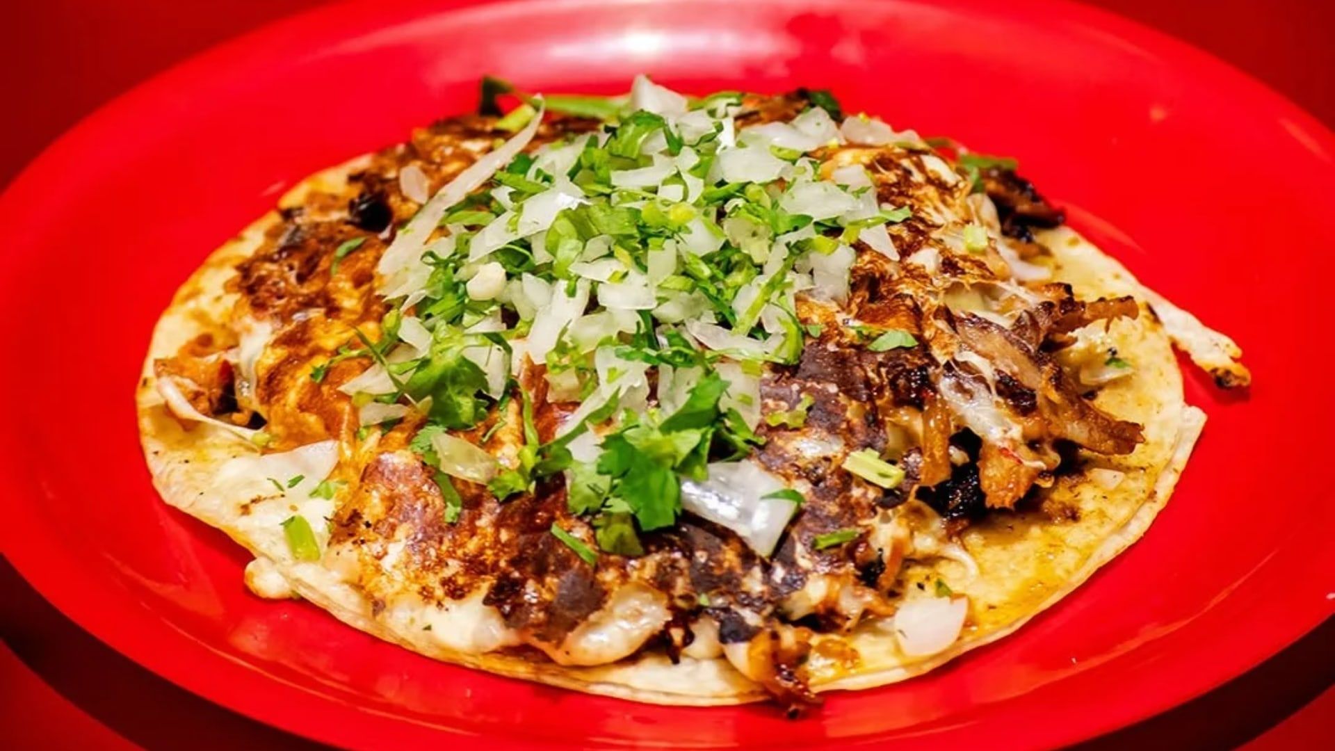 Taco de Tacos Chilaca con cebolla y cilantro sobre un plato rojo